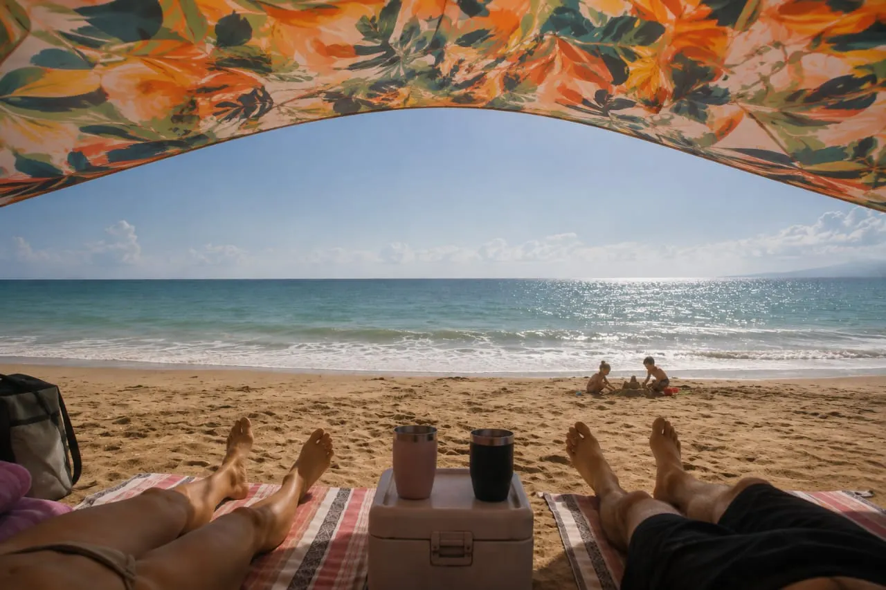 Vista desde debajo de una carpa Shadow hacia el mar con dos personas descansando.